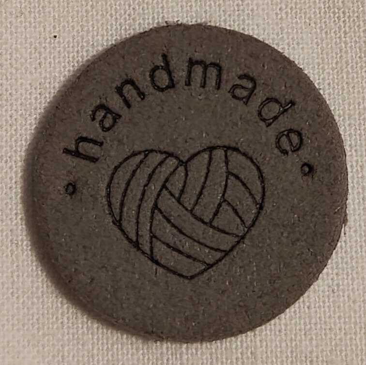 Keinonahkainen pyöreä harmaa handmade-merkki.