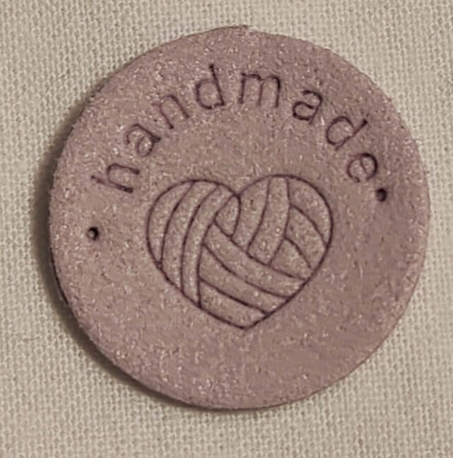 Keinonahkainen pyöreä vaalea lila handmade-merkki.